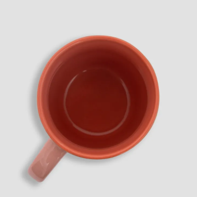 Caneca de cerâmica vermelha alaranjada vista de cima com asa rosa clara sobre fundo cinza
