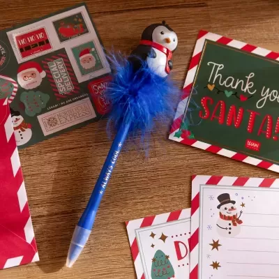 Caneta decorativa com tema natalício e etiquetas de Natal sobre mesa de madeira