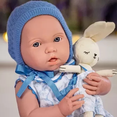 Boneca bebé com touca azul e vestido azul, segurando um boneco coelho de tecido