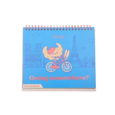 Calendário de mesa 2026 com ilustração de croissant a andar de bicicleta e monumentos franceses