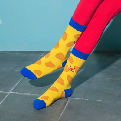 Meias amarelas com manchas alaranjadas e detalhe de gato, com calças vermelhas e chão cinzento