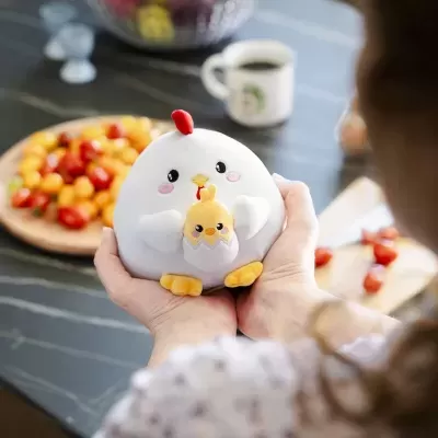 Brinquedo de pelúcia galinha com pintainho nas mãos em cozinha