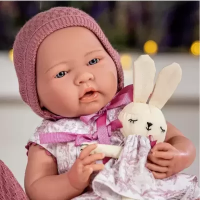 Boneca bebé realista com touca rosa segurando coelho de pano com vestido branco e rosa