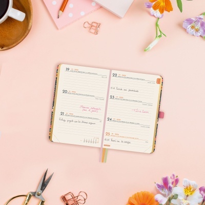 Agenda semanal aberta sobre mesa cor-de-rosa com texto escrito, flores e clipes de papel