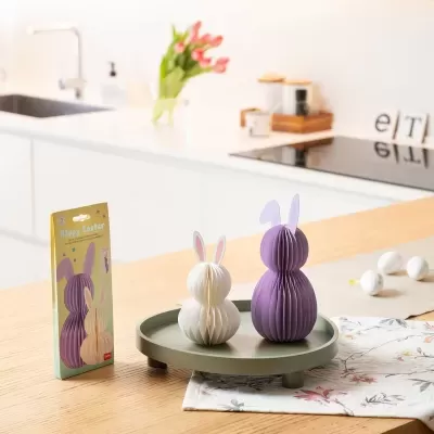 Decoração de Páscoa com coelhos de papel dobrado branco e roxo numa bandeja verde sobre mesa de madeira