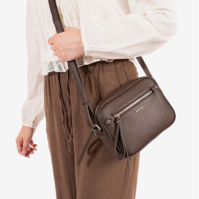 Mala castanha de pele com fecho prateado e bolso exterior, usada ao ombro.