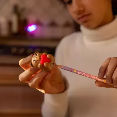 Apontador em forma de ursinho castanho a segurar um coração vermelho e lápis colorido com frase visível