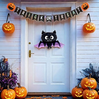 Decoração de Halloween numa porta branca com guirlanda TRICK OR TREAT, morcego e várias abóboras iluminadas