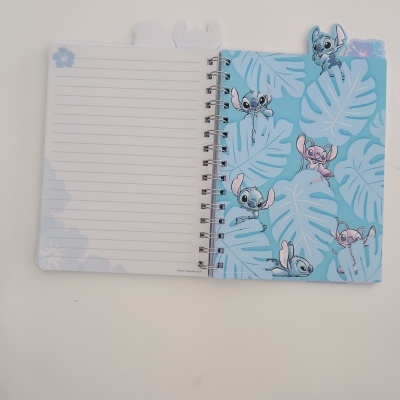 Caderno de argolas azul com folhas tropicais e personagens Stitch aberto sobre uma superfície branca.