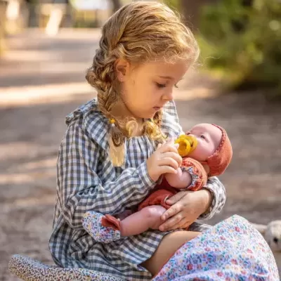 Menina com vestido xadrez segurando boneca com roupinha e touca cor de tijolo