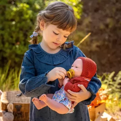 Menina segurando boneca realista vestida de vermelho ao ar livre