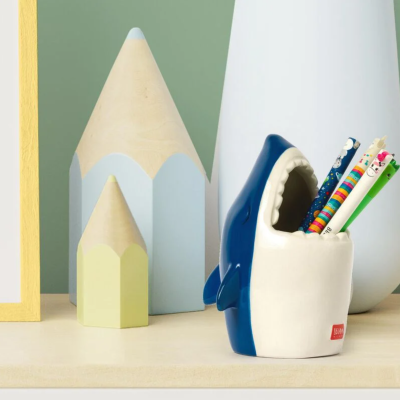 Suporte de canetas em forma de tubarão azul e branco com lápis coloridos junto com lápis decorativos grandes e vaso branco