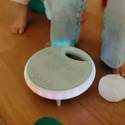 Coluna portátil redonda cinzenta com luzes LED coloridas e orifício para transporte no chão de madeira