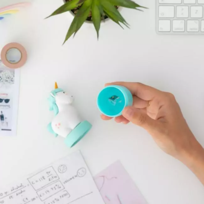 Apontador unicórnio azul e branco sobre mesa branca com objetos