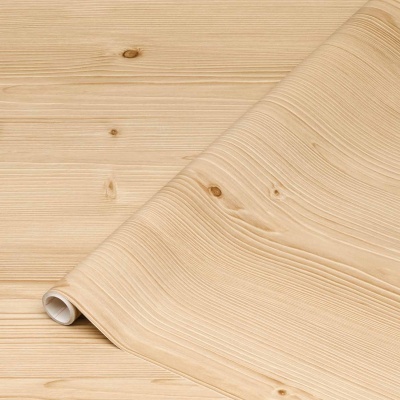 Rolo de papel de parede autocolante com padrão de madeira clara desenrolado sobre superfície de madeira