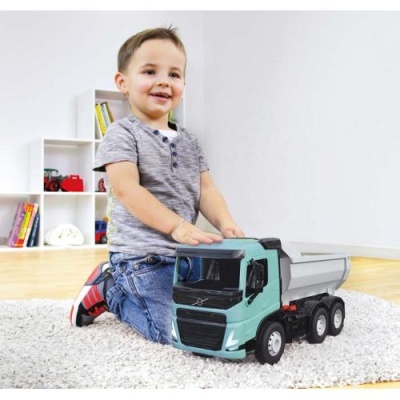 Criança a brincar com camião de brinquedo Volvo verde-água em sala com tapete branco