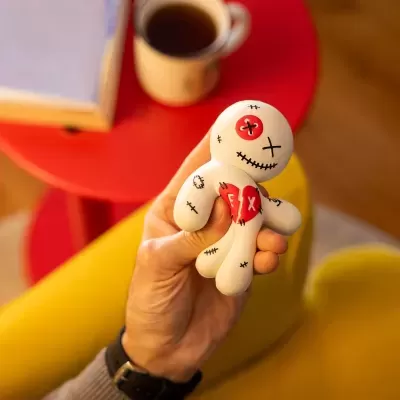 Boneco de vinil com detalhes em vermelho e preto segurado por uma mão com mesa vermelha e cadeira amarela ao fundo