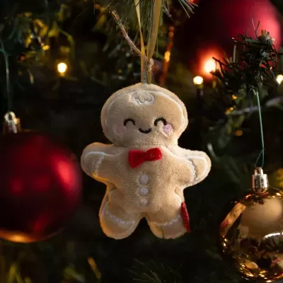Enfeite de Natal em forma de homem de pão-de-espécie bege com laço vermelho pendurado numa árvore de Natal