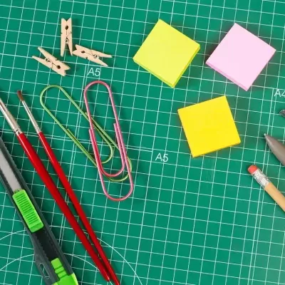 Artigos de escritório e de arte dispostos sobre tapete de corte verde com marcações A5 e A4