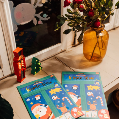 Embalagens de autocolantes natalícios para janelas Windo-Wow numa superfície branca junto a janela decorada