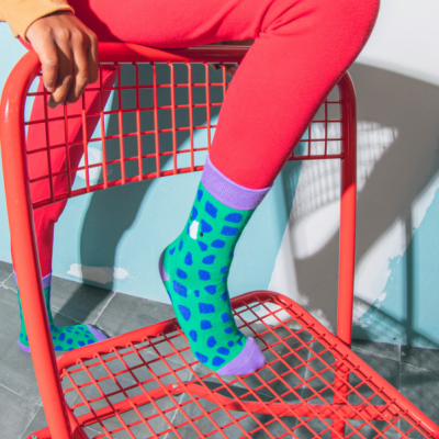 Pessoa com meias verdes com padrão azul sentada numa cadeira vermelha de grade