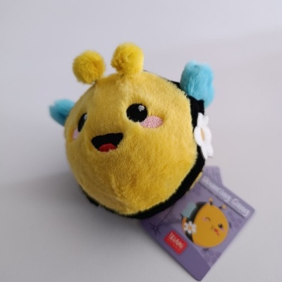 Pelúcia redonda amarela em forma de abelha com antenas e asas coloridas e etiqueta púrpura.