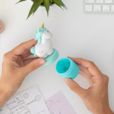 Figura de unicórnio azul e branco desmontada em duas partes sobre mesa branca com teclado e papéis