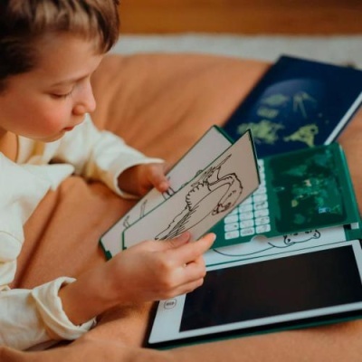 Criança a interagir com tablet e cartões com desenhos de dinossauros