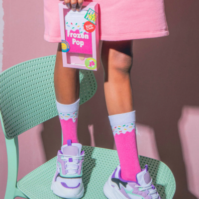 Menina com vestido rosa, meias cor-de-rosa e ténis coloridos segurando caixa Frozen Pop