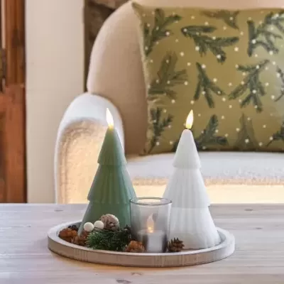 Velas em forma de árvore de Natal em verde e branco num tabuleiro com enfeites sobre mesa de madeira clara