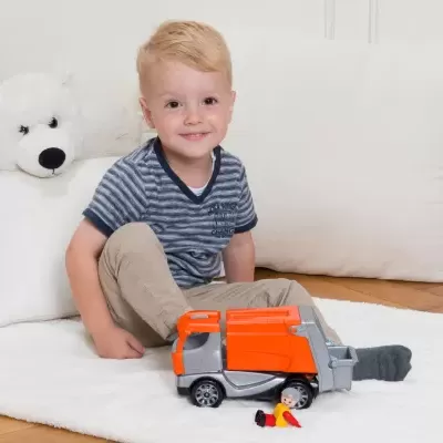 Criança loira a brincar com camião de lixo de brinquedo sobre tapete branco