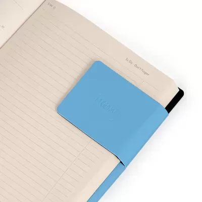 Caderno aberto com clipe de papel azul claro com relevo a segurar as páginas