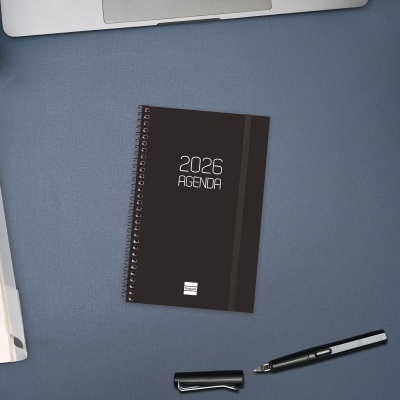 Agenda 2026 preta com espiral e caneta preta sobre mesa azul
