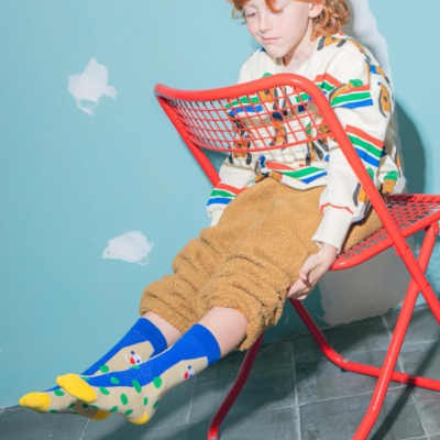 Criança com camisola riscada e calças felpudas sentada numa cadeira vermelha numa sala azul