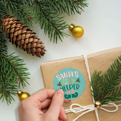 Mão a colocar autocolante de Natal num pacote com decoração de pinheiro e sino