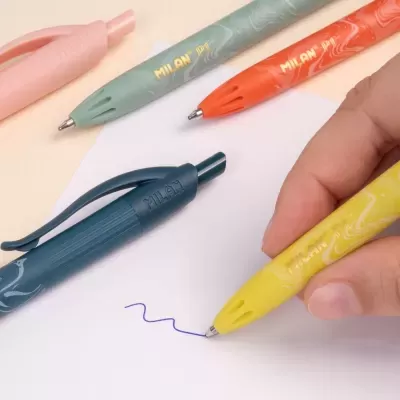 Esferográficas MILAN coloridas com corpo texturizado em uso numa folha branca