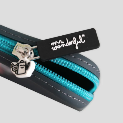 Estojo preto com zíper azul e puxador metálico com desenho de livro com asas