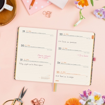 Agenda aberta com anotações rodeada por flores e acessórios de papelaria