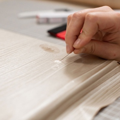 Mão a aplicar cola numa superfície de madeira clara com textura