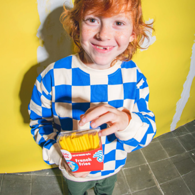 Criança com camisola azul e branca aos quadrados segurando caixa de batatas fritas vermelha