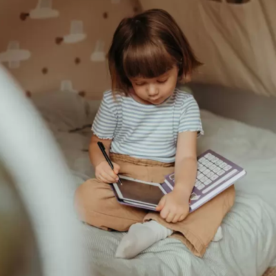 Criança usa tablet sólido roxo com teclado branco sentada numa cama