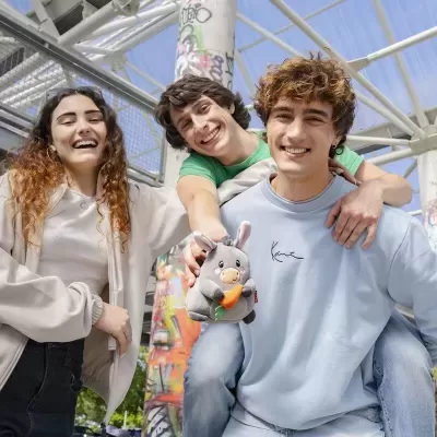Três jovens sorridentes em ambiente urbano segurando peluche de coelho