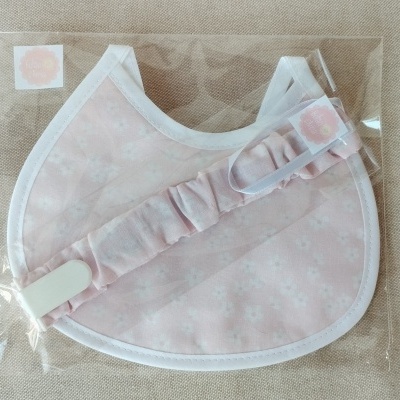 Babete rosa claro com padrão floral e fita, embalados em plástico transparente com letra M