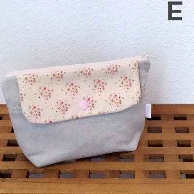 Bolsa pequena cinzenta com aba de flores cor-de-rosa num fundo creme