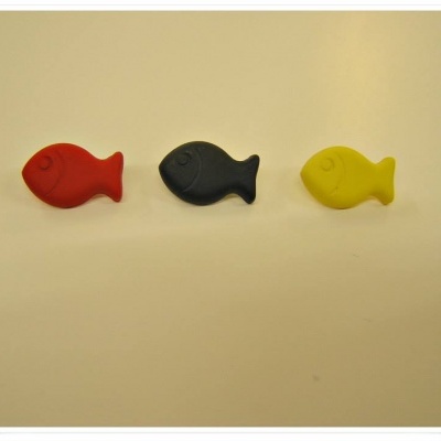 Ímanes em forma de peixe coloridos (vermelho, preto, amarelo) sobre superfície branca