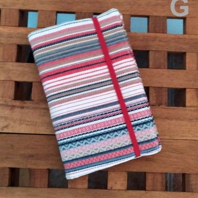 Caderno com capa de tecido colorido e elástico vermelho numa mesa de madeira.