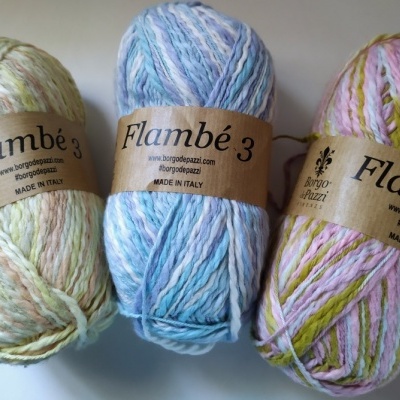 Três novelos de lã coloridos da marca Flambé 3 com rótulos marrons