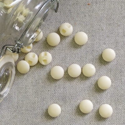 Contas de pérola brancas dispersas em tecido cinza com frasco de vidro aberto e texto 'Pérola'
