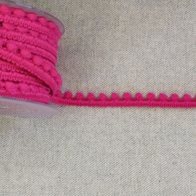 Rolo de fita decorativa rosa forte com pompons pequenos sobre tecido cinza