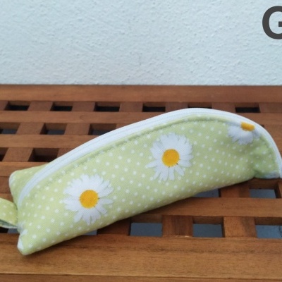 Estojo creme com padrão de margaridas brancas sobre madeira com parede branca